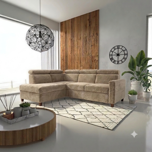 A beige L-shaped sectional sofa in a modern living room setting, styled with a patterned rug, a round wooden coffee table, a black wire pendant light, and potted plants.