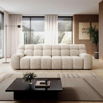 A modern beige sofa in a bright, contemporary living room with light wood floors, a black marble coffee table, and large windows with sheer curtains.