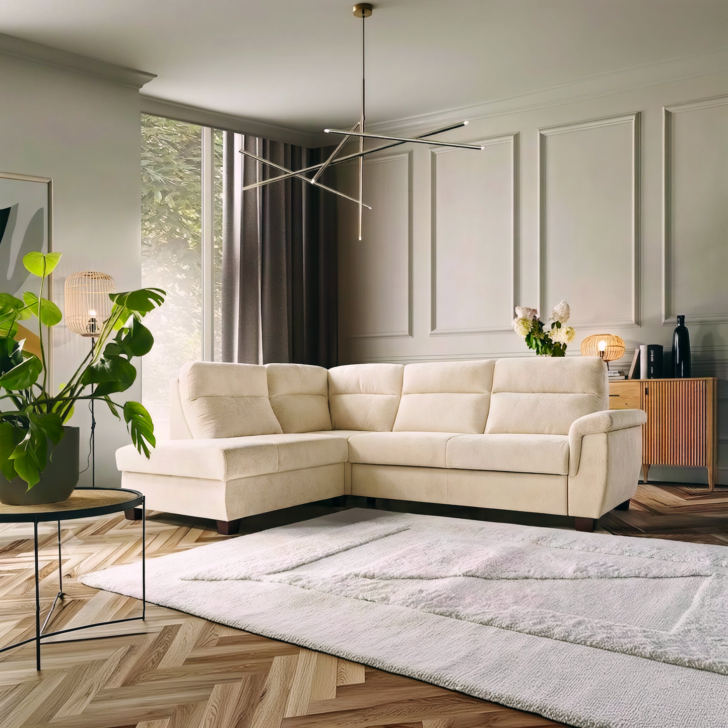 A modern L-shaped sectional sofa upholstered in warm off-white fabric, styled in a contemporary living room with a light wood herringbone floor, a large white rug, and neutral paneled walls.