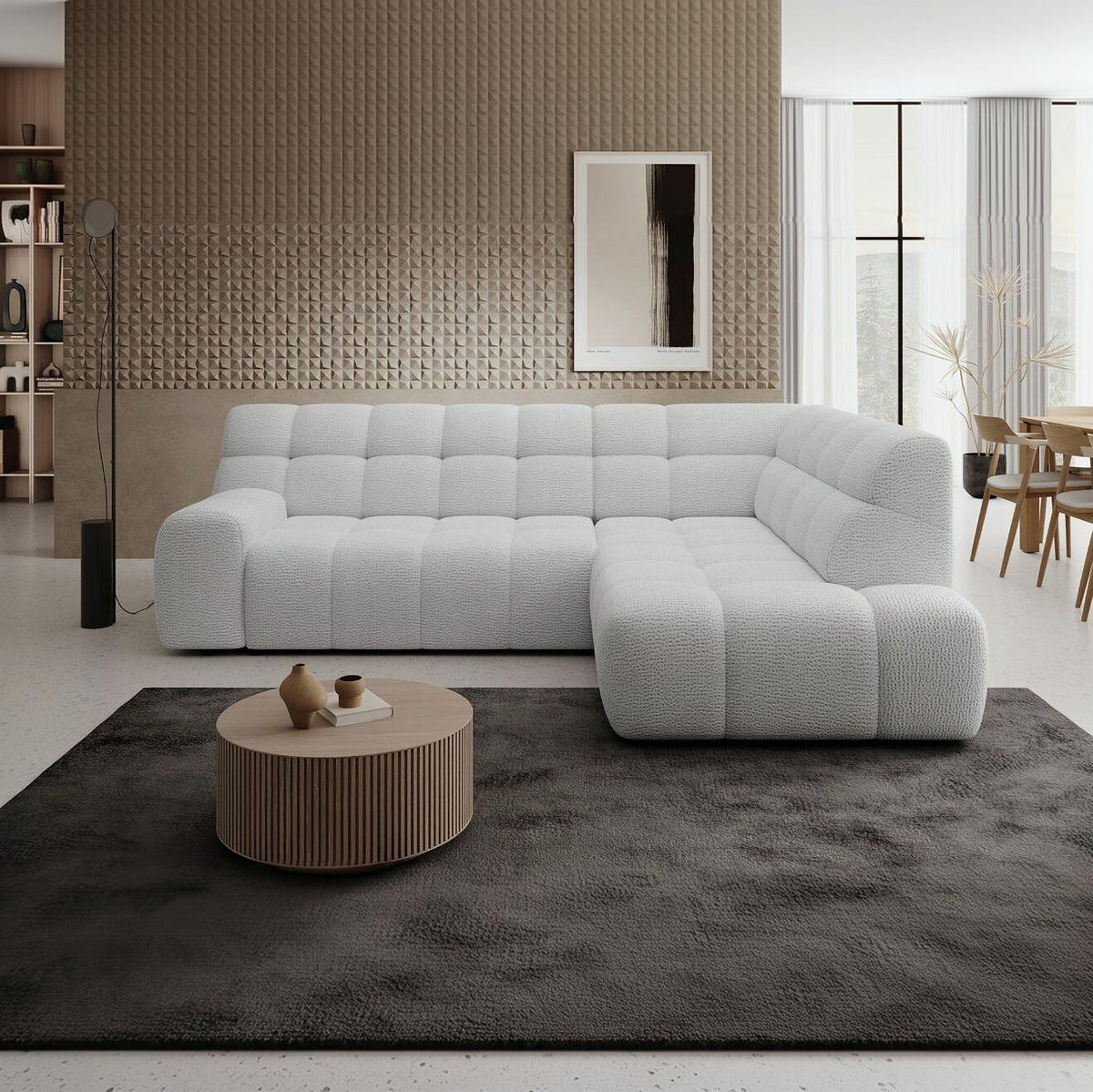A modern light gray tufted sectional sofa in a styled living room setting, placed on a dark gray rug with a round ribbed coffee table in front.