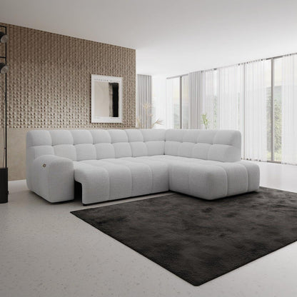 A modern white tufted sectional sofa in a minimalist living room setting with a dark gray rug, textured wall, and large windows with sheer curtains.