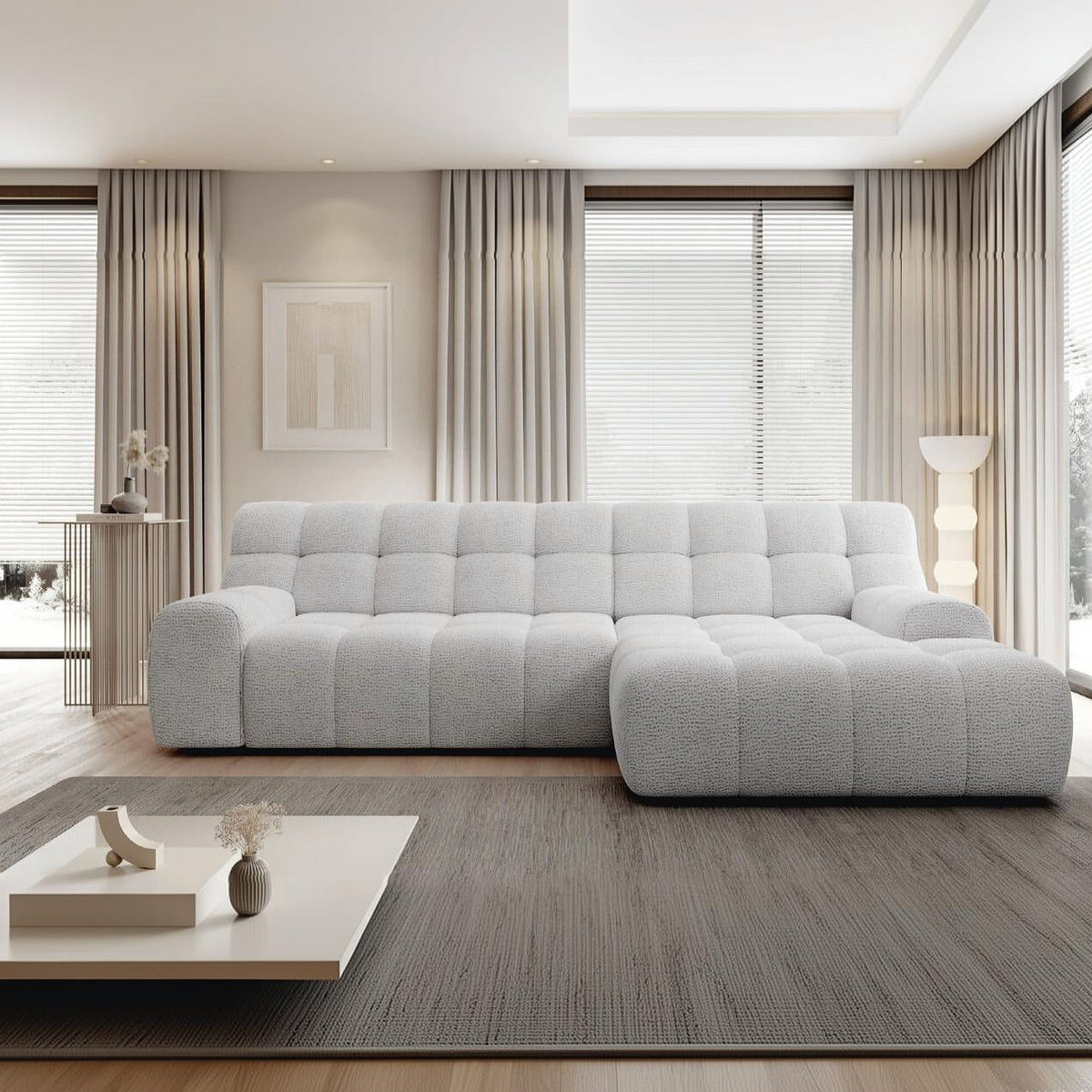 A modern light gray tufted sectional sofa in a bright, contemporary living room with beige curtains, a gray rug, and a low white coffee table.
