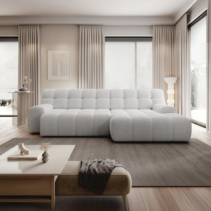 A modern sectional sofa in a light gray bouclé fabric, styled in a contemporary living room with beige curtains, a wooden coffee table, and a gray rug.