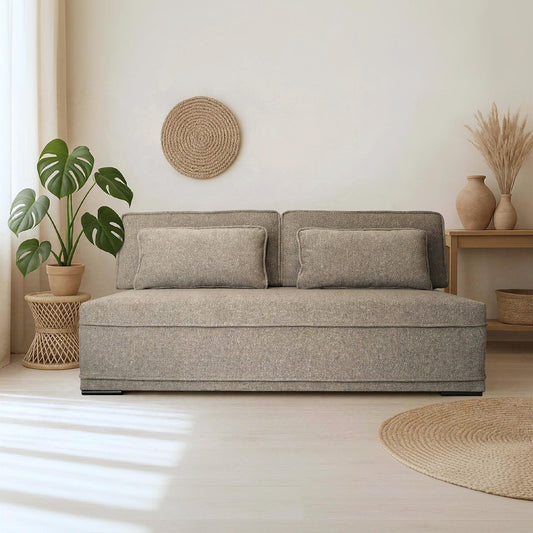A modern two-seater sofa in a textured light gray fabric, styled in a bright, minimalist room with a potted monstera plant, a wooden side table, and a woven wall decor piece.